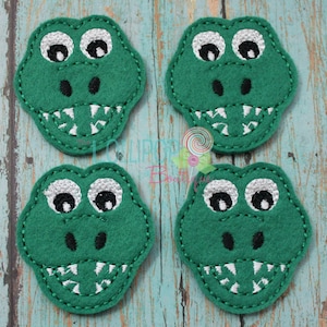 May include: Four green felt alligator face appliques with white teeth, black eyes, and white pupils.