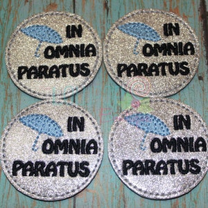 May include: Four silver glitter round coasters with black stitching around the edges. Each coaster features a blue embroidered umbrella and the text "In Omnia Paratus" in black.