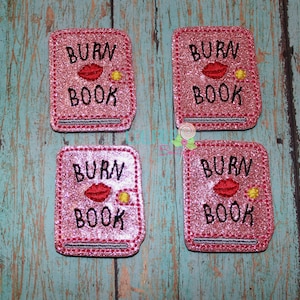 May include: Four pink glitter iron-on patches with the text "BURN BOOK" and a red lip print.