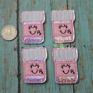 May include: Four pink pill bottle shaped iron-on patches with a smiling face and the letters "RX" on each. The patches have a glittery finish.