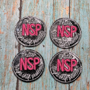 May include: Four black and silver round patches with the text "NSP" in pink embroidery.