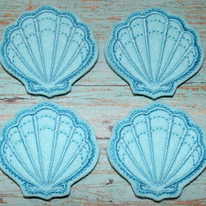 May include: Four light blue felt seashell shapes with a white outline. The seashells are stitched with a decorative pattern.