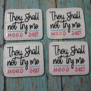 May include: Four white square patches with a glittery finish. Each patch has black text that reads "Thou shall not try me" with a pink and blue line underneath. The text "MOOD 2487" is printed in pink below the line.