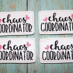 May include: Four white rectangular patches with black embroidery that reads "chaos coordinator" with two pink hearts on each patch.