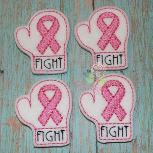 May include: Four white fabric boxing glove patches with pink ribbon embroidery and the word "FIGHT" in black. The patches are outlined with pink stitching. The background is a light blue and teal wood grain.