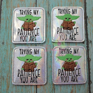 May include: Four silver and iridescent iron-on patches with a green cartoon character and the text "Trying my patience you are".