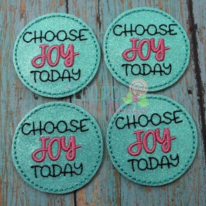 May include: Four round teal patches with the words "CHOOSE JOY TODAY" embroidered in black and pink. The patches have a glittery texture and a stitched border. The patches are arranged in a square.