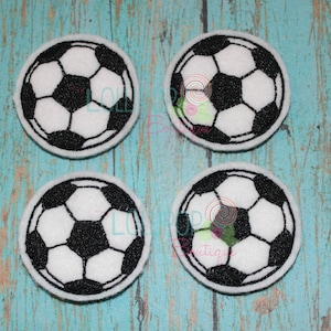 May include: Four white felt circles with black embroidered soccer balls. Each circle is approximately 2 inches in diameter.
