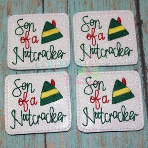May include: Four white, glittery square patches with the text "Son of a Nutcracker" in green and red script. Each patch features a green elf hat with yellow stripes and a red feather.