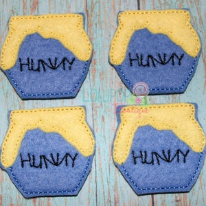 May include: Four felt honey pot ornaments with a yellow top and blue base. Each pot has the word "Hunny" embroidered in black.