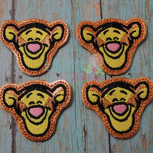 May include: Four embroidered iron-on patches featuring Tigger from Winnie the Pooh. Each patch is orange, yellow, and black with a glittery finish.