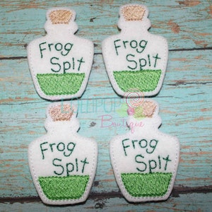 May include: Four white felt bottle-shaped patches with embroidered tan corks and green liquid bases. Each patch features the dark green embroidered text "Frog Spit" centered on the white background. The edges are stitched with white thread.