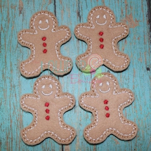 May include: Four brown felt gingerbread man ornaments with white stitching and red button details.