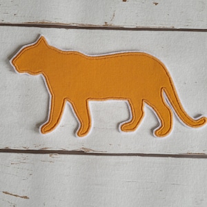 Könnte beinhalten: Orangefarbene Filzapplikation einer Katzensilhouette auf weißem Holzgrund.