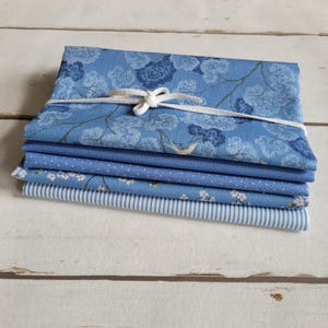 Könnte beinhalten: Ein Stapel aus sechs blauen Stoffquadraten mit verschiedenen Mustern. Der oberste Stoff hat ein Blumenmuster, der zweite Stoff ist einfarbig blau, der dritte Stoff hat ein kleines weißes Punkte-Muster, der vierte Stoff hat ein kleines weißes Blumenmuster, der fünfte Stoff hat ein weiß-blaues Streifenmuster und der unterste Stoff ist einfarbig blau.