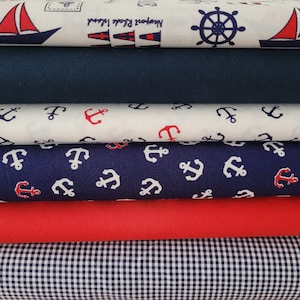 Könnte beinhalten: Ein Stapel Stoffe im maritimen Stil. Die Stoffe zeigen Muster von Segelbooten, Ankern und Steuerrädern in Rot, Weiß und Marineblau. Ein Stoff ist einfarbig marineblau, ein anderer einfarbig rot, und ein letzter Stoff hat ein schwarz-weißes Vichy-Muster.