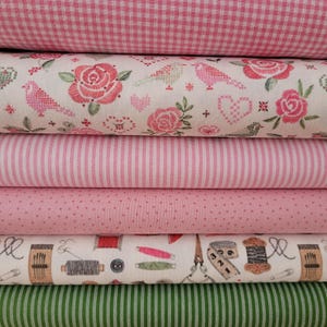 Könnte beinhalten: Ein Stapel Stoffballen in verschiedenen rosa- und grüntönen. Die Stoffe umfassen Karomuster, Blumenmuster, Streifen und Punkte. Ein Stoff zeigt Illustrationen zum Thema Nähen.