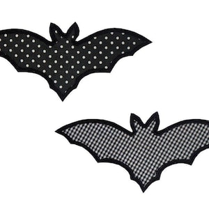 Könnte beinhalten: Zwei schwarze Stoff-Fledermäuse mit unterschiedlichen Mustern. Eine Fledermaus hat weiße Punkte und die andere ein schwarz-weißes Karomuster.