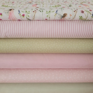 Könnte beinhalten: Ein Stapel Stoffrollen in verschiedenen Mustern und Farben. Die oberste Schicht zeigt ein Blumendesign mit Feen. Darunter befinden sich rosa gestreifte, grüne gepunktete, einfarbige rosa und gepunktete rosa Stoffe. Die unterste Schicht ist ein einfarbiger grüner Stoff.