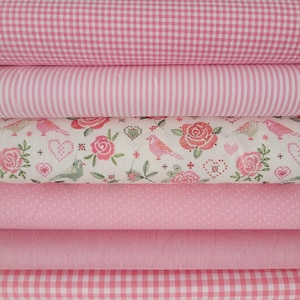 Könnte beinhalten: Ein Stapel aus sechs gefalteten Stoffballen in verschiedenen Rosa- und Weißtönen. Die Muster umfassen ein rosa-weißes Gingham-Karomuster, dünne vertikale rosa Streifen, einen Blumendruck mit Vögeln und Herzen, kleine weiße Punkte, einfarbiges Rosa und ein größeres rosa-weißes Gingham-Karomuster.