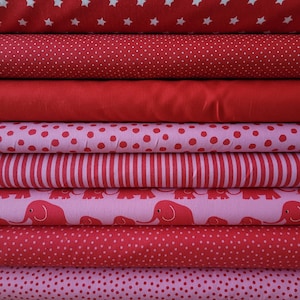 Könnte beinhalten: Ein Stapel roter und rosa Stoffe mit verschiedenen Mustern. Die Stoffe zeigen weiße Sterne, Punkte, Streifen und Elefantenmotive. Die Stoffe sind ordentlich gefaltet und gestapelt und zeigen eine Vielzahl von Designs.
