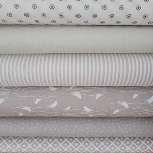Könnte beinhalten: Ein Stapel aus sechs gefalteten Stoffballen mit verschiedenen Mustern in neutralen Farbtönen. Die Muster umfassen kleine dunkelgraue florale Kreise, einfarbiges Beige, beige-weiße vertikale Streifen, weiße Vögel auf Beige, kleine weiße Punkte und weiße Rauten.