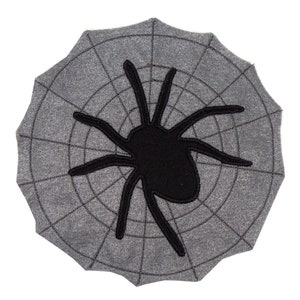 Könnte beinhalten: Ein grauer Stoff-Spinnennetz mit einer schwarzen Spinne in der Mitte.