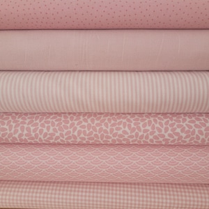 Könnte beinhalten: Ein Stapel verschiedener rosa Stoffmuster. Die Stoffe weisen verschiedene Muster auf, darunter Punkte, Streifen und florale Designs. Die Farbpalette besteht aus sanften und mittleren Rosatönen und schafft eine optisch ansprechende Anordnung.
