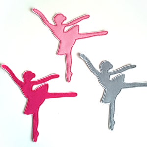 Könnte beinhalten: Drei Ballerina-Silhouetten aus Filz, eine rosa, eine hellrosa und eine graue. Die Ballerinas sind alle in der gleichen Pose, mit einem ausgestreckten Bein und dem anderen, das am Knie gebeugt ist.