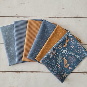 Op de afbeelding: Een verzameling van zes gevouwen stofstalen met diverse patronen, waaronder blauw met witte stippen, blauw-witte strepen, effen mosterdgeel, mosterdgeel met witte stippen en een blauwe print met vossen en florale motieven.