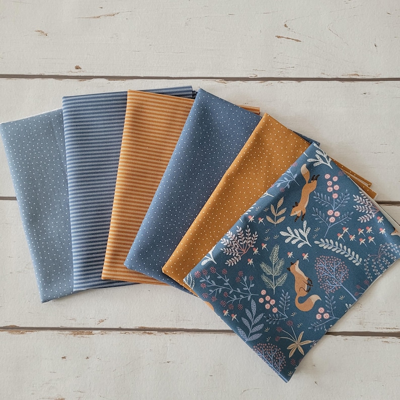 Op de afbeelding: Een verzameling van zes gevouwen stofstalen met diverse patronen, waaronder blauw met witte stippen, blauw-witte strepen, effen mosterdgeel, mosterdgeel met witte stippen en een blauwe print met vossen en florale motieven.