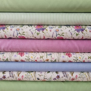 Könnte beinhalten: Ein Stapel aus acht gefalteten Stoffballen mit abwechselnden einfarbigen und floralen Mustern. Die Kollektion umfasst Salbeigrün, grün-weiße Streifen, einen cremefarbenen Blumendruck, einfarbiges Mauve, einen Wildblumendruck, einfarbiges Immergrün, einen lavendelfarbenen Blumendruck und grüne Streifen.