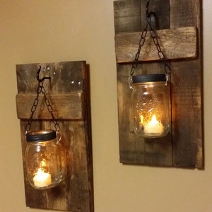 Pu&ograve; includere: Due applique da parete in legno rustico con barattoli di vetro sospesi e candele. Ogni applique &egrave; realizzata in legno riciclato e ha un gancio e una catena in metallo per tenere il barattolo.