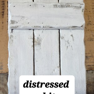 May include: Distressed white wooden shutters with a rustic, weathered look. The shutters are painted white with a distressed finish, giving them a vintage feel.