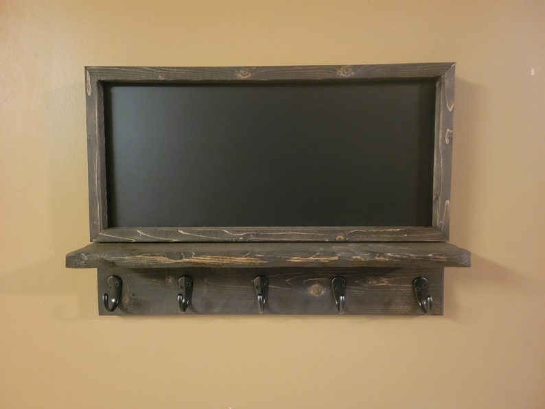 May include: A dark brown wooden shelf with a chalkboard above it. The shelf has four black metal hooks and a rustic finish.