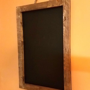May include: A rustic wooden framed chalkboard with a rope hanger. The chalkboard is black and the frame is a dark brown wood.