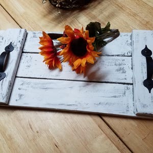 May include: White wooden serving tray with black metal handles. The tray has a distressed white paint finish and is decorated with a bouquet of orange and red sunflowers.