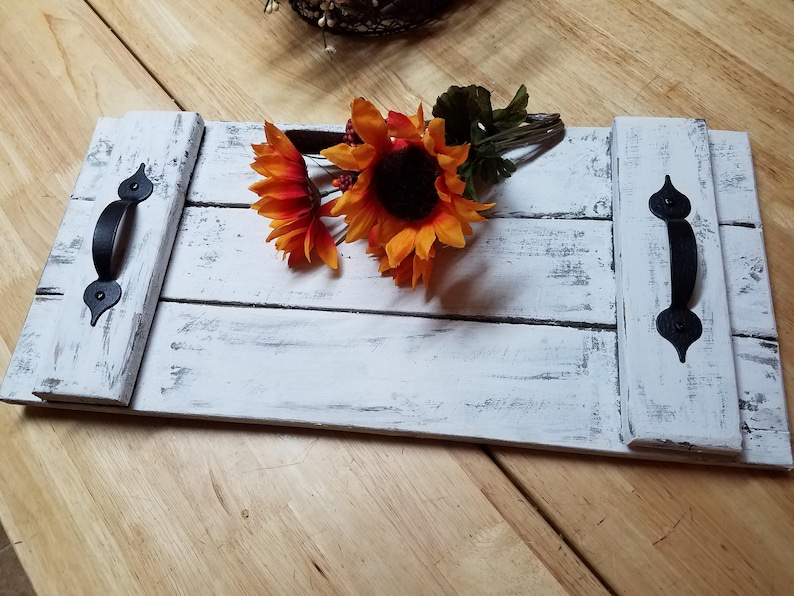 May include: White wooden serving tray with black metal handles. The tray has a distressed white paint finish and is decorated with a bouquet of orange and red sunflowers.
