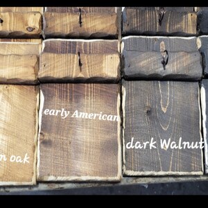 May include: Close-up of wooden signs with different wood stain colors. The signs are labeled "Golden Oak", "Early American", "Dark Walnut", and "Ebony".
