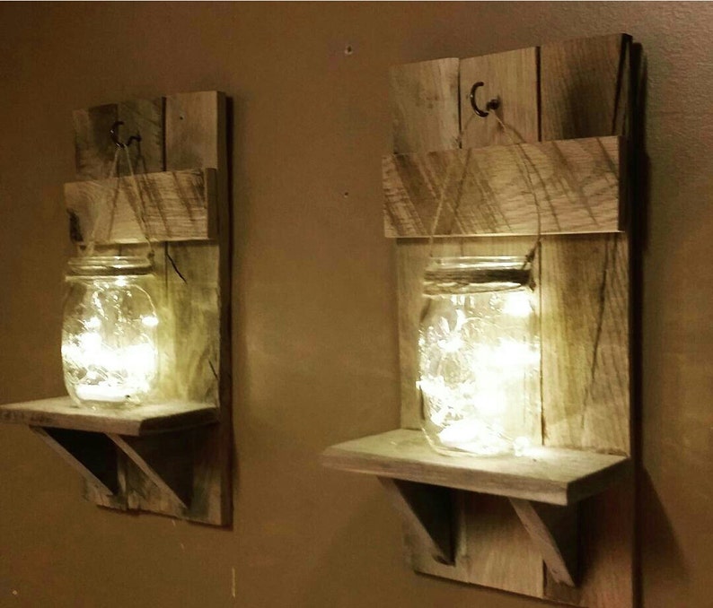 May include: Two rustic wooden wall shelves with a mason jar on each shelf. The jars are filled with fairy lights and hung from a hook on the shelf.
