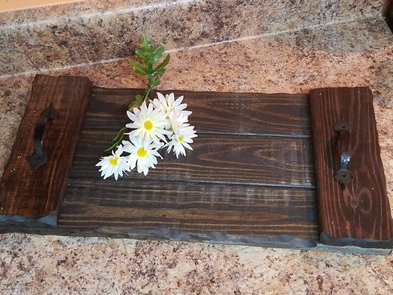 May include: A wooden serving tray with two black metal handles. The tray has a dark brown stain and is made of reclaimed wood. A bouquet of white daisies is on the tray.