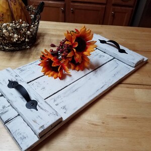 May include: Whitewashed wooden tray with black metal handles. The tray is made of reclaimed wood and has a rustic look. A bouquet of orange and red sunflowers is on top of the tray.
