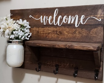 Letrero de bienvenida rústico de madera, estante con tarro, ganchos para abrigos