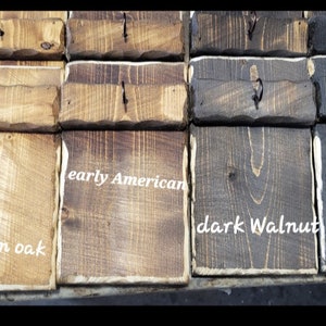 May include: Close-up of wooden blocks stained in different colors, including golden oak, early American, dark walnut, and ebony. Each block has a small metal hook.