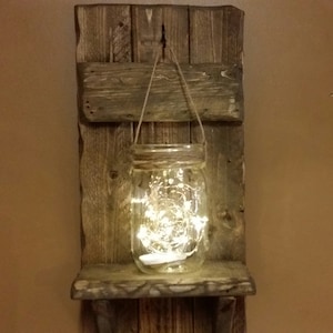 May include: A rustic wooden shelf with a hanging mason jar filled with fairy lights. The shelf is made of reclaimed wood and has a distressed finish.