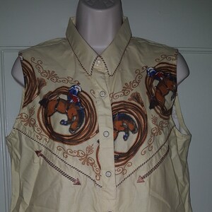 May include: A sleeveless, light yellow button-down shirt with a western-themed print featuring brown horses and rope designs. The shirt has a pointed collar and a button-up front.