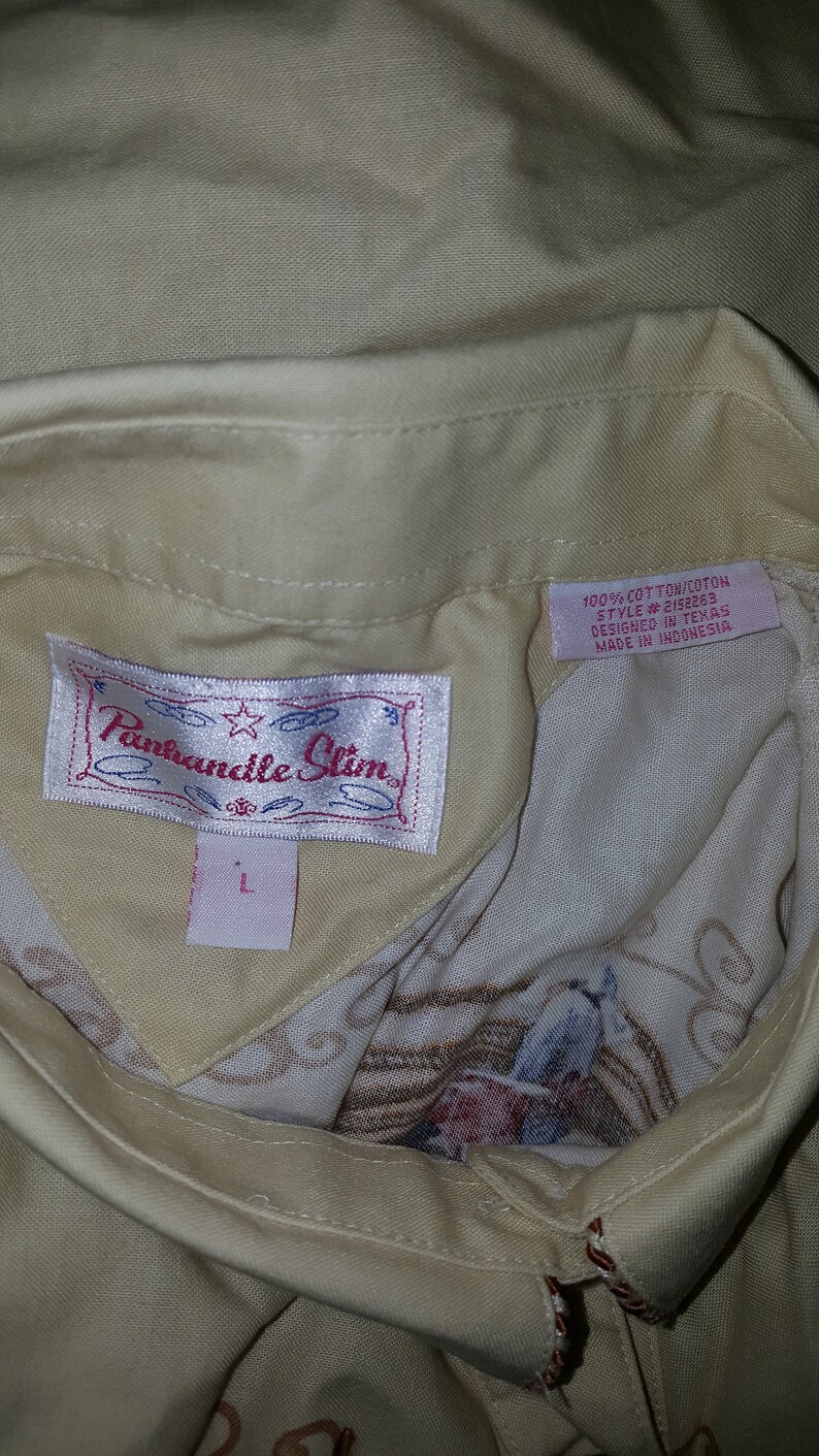 May include: A beige button-down shirt with a white label that says "Panhandle Slim" and a pink label that says "100% Cotton/Coton Style #2152263 Designed in Texas Made in Indonesia".