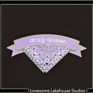 May include: A purple and gold enamel pin with a bandana design and the text "drag queen".