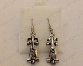 May include: A pair of silver earrings featuring a detailed design of a race car. The earrings are on a white background.
