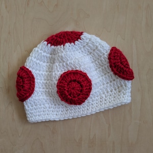 May include: White crocheted hat with red crocheted circles. The hat is shaped like a mushroom.
